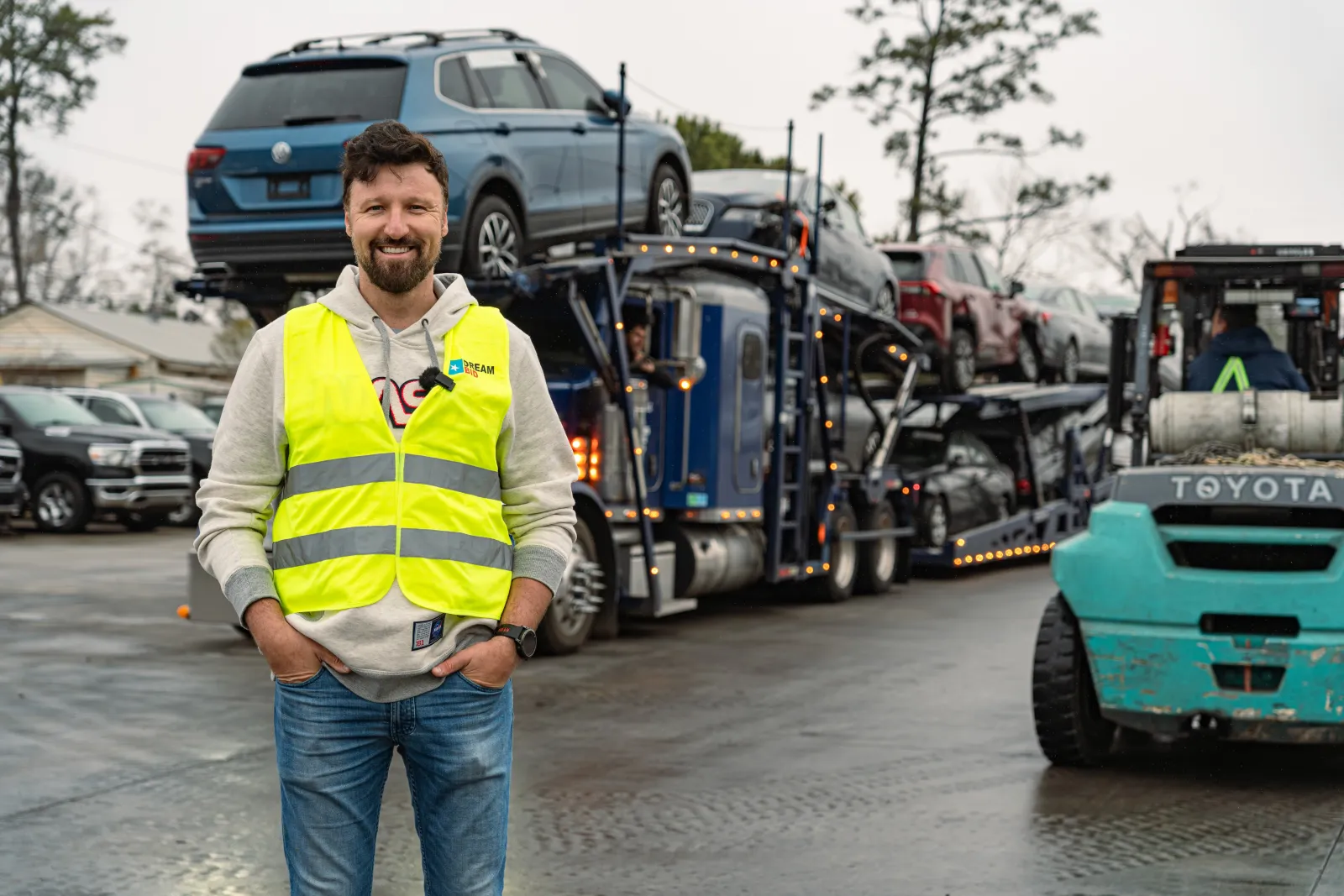Pracownik DreamBid w firmowej kamizelce odblaskowej na placu w USA, przed załadowaną lawetą z autami